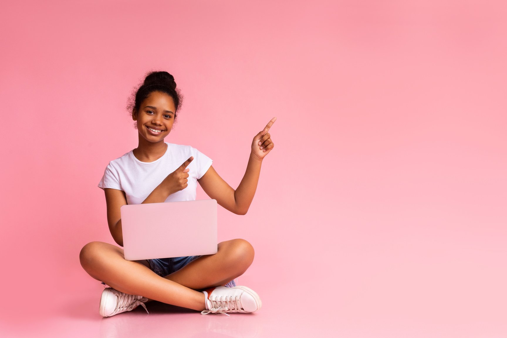 Excited teenage girl with laptop pointing at pink background